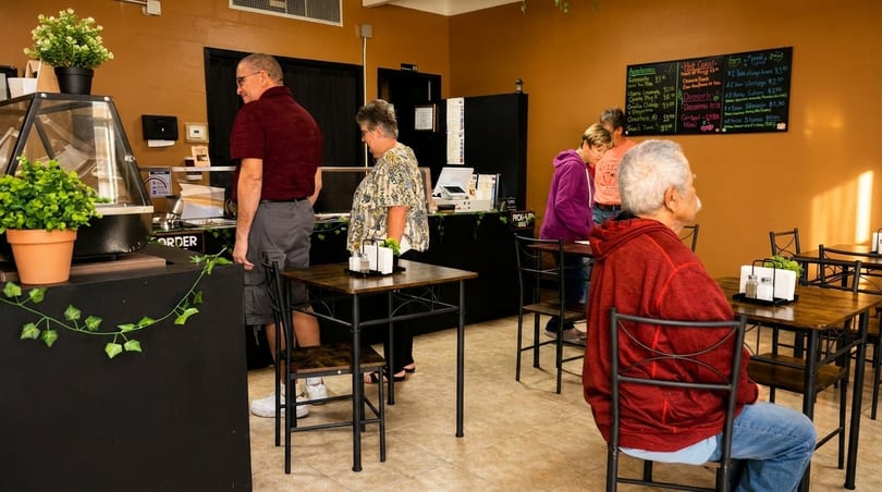 Customers ordering and dining in a casual restaurant with a menu board on the wall.